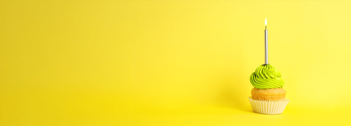 Image of cupcake with a candle in it against a banana yellow background.