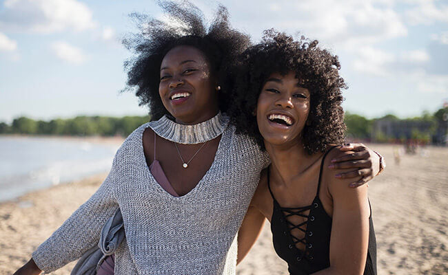 Image of two Black women laughing as they walk on the beach | Celebrating beauty at every age and season | Ageless beauty