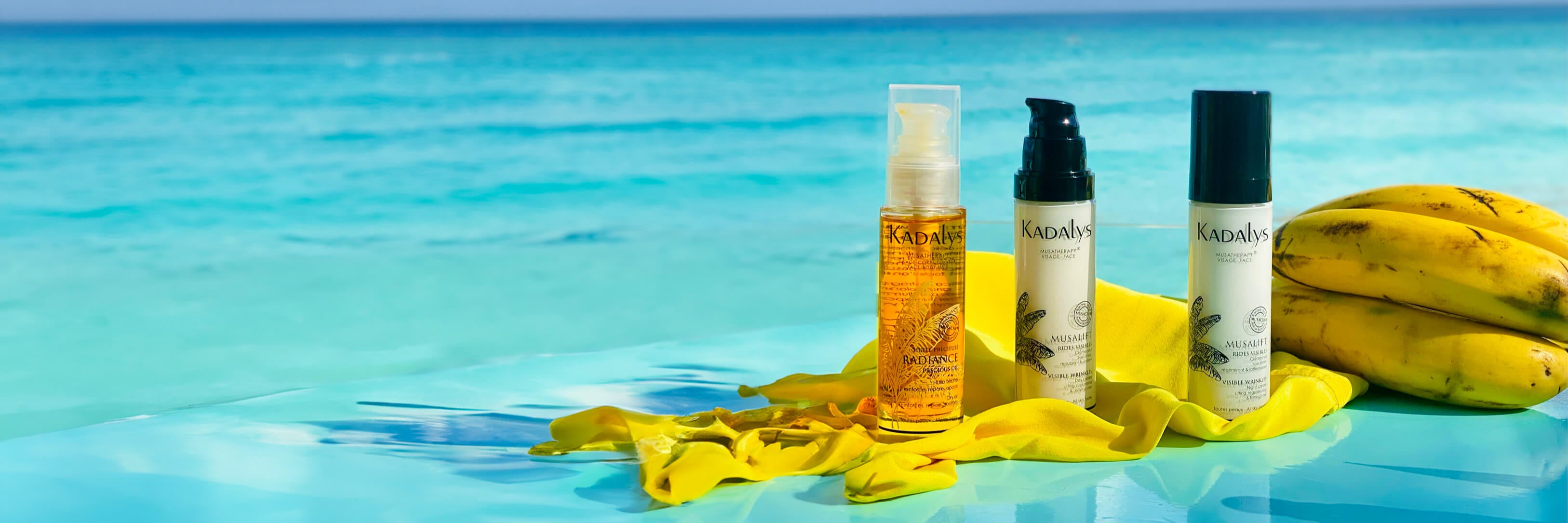 Image of Kadalys products next to banana on a yellow beach towel with blue Caribbean water in the background | Kadalys effective natural skincare products made from bananas