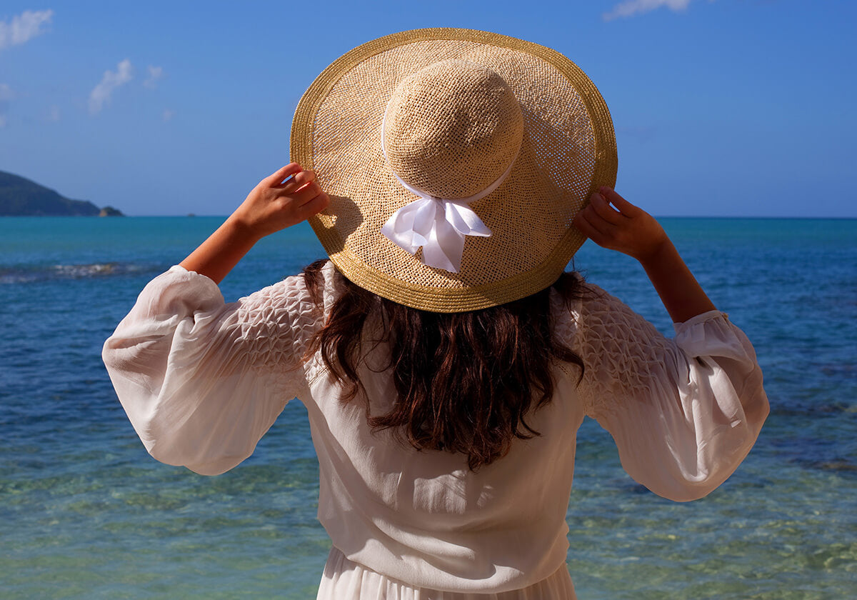 Image of woman wearing straw hat and standing in front of Caribbean Sea