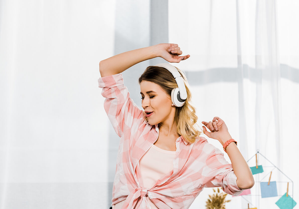 Woman dancing while listening to headphones in front of a window with white curtains
