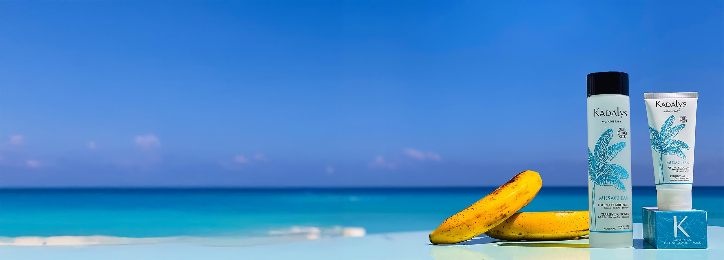 Image of yellow bananas and Kadalys toner and exfoliator in front of sea and blue sky | Sustainable skincare made from upcycled banana bio-actives