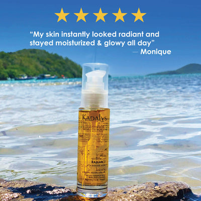 Image of face oil in front of Caribbean sea with green tress in the distant background.  Caption reads 5 stars. My skin  instantly looked radiant and stayed moisturized & glowy all day.